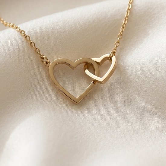 Goudkleurige ketting met twee in elkaar grijpende open hartjes op een glanzende witte zijden ondergrond.
