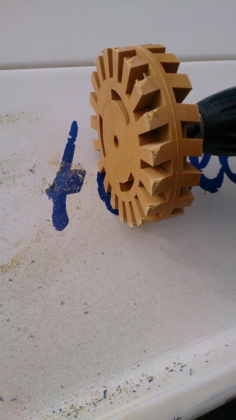 Gele rubberen caramelschijf, op een boormachine, verwijdert blauwe inkt van een wit oppervlak. Verwijderde schraapsels liggen op het oppervlak.