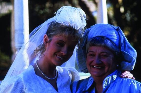 Bruid met sluier en parelketting naast een vrouw met blauwe hoed.
