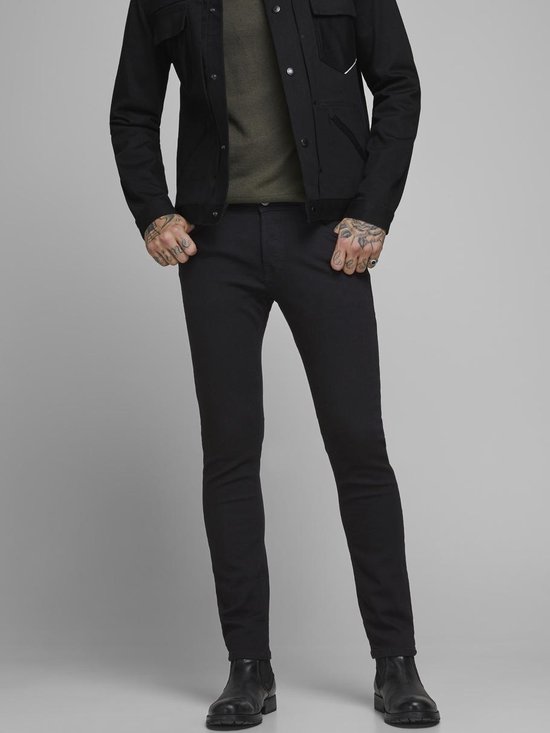 Man in zwarte skinny jeans en zwarte jas, met tatoeages op de handen.