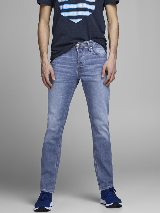 Man in een blauwe spijkerbroek en t-shirt, staand.
