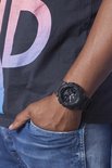 Zwarte G-Shock horloge om de pols van een man, met een detail van een t-shirt en jeans.