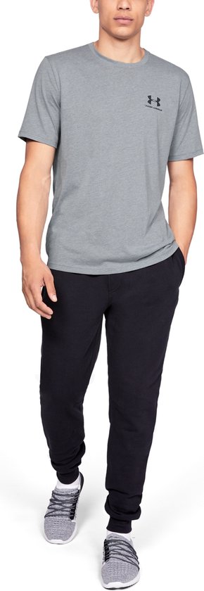 Model loopt naar voren in een grijs Under Armour shirt met korte mouwen en een zwart logo op de borst.