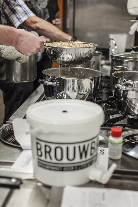 Gezicht op een keuken met kookgerei, een witte emmer en een persoon die graan zeeft.