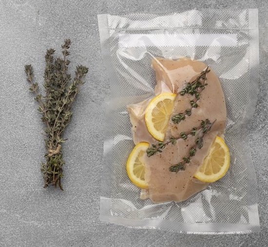 Un filet de poulet avec du citron et du thym dans un sac sous vide, à côté d'une botte de thym.