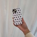 Hand die een witte telefoonhoes met zwarte stippen vasthoudt.