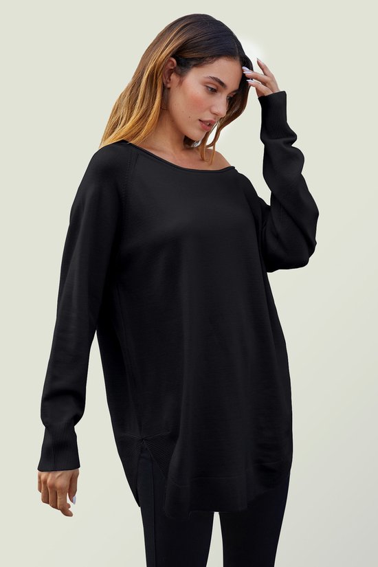 Model draagt een oversized zwarte gebreide trui met een wijde halslijn die over één schouder valt.