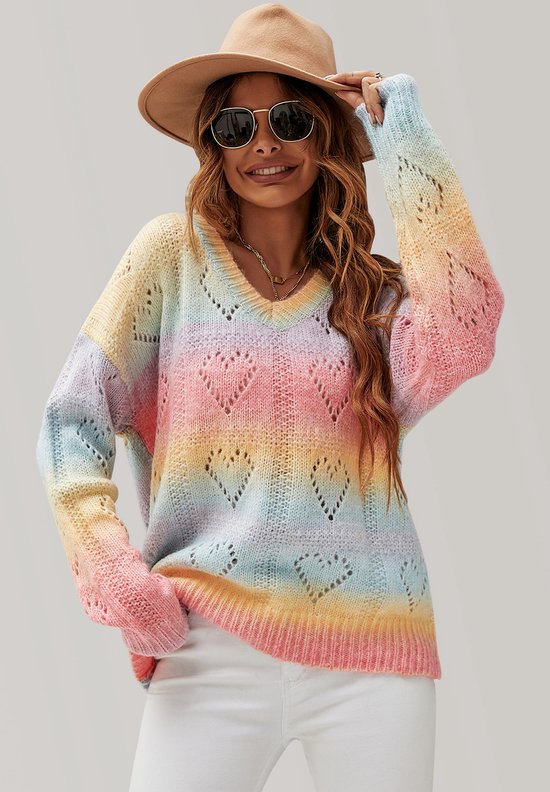 Een model draagt een trui met V-hals en regenboogkleuren en een opengewerkt hartpatroon. Ze draagt een hoed.