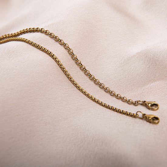 Twee gouden schakelarmbanden met karabijnsluitingen, liggend op een crèmekleurige stof.