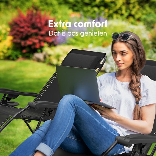 Vrouw met zonnebril op, zittend in een zwarte ligstoel met een laptop in de tuin.