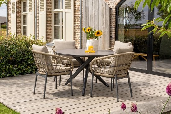 Een ronde tafel met vier gevlochten stoelen op een houten terras, met zonnebloemen op tafel.