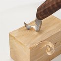 Een gebogen houtsnijmes wordt gebruikt om krullen van een houten blok te schrapen.