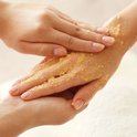 Een hand wordt ingemasseerd met een gele bodyscrub. De textuur van de scrub is zichtbaar.