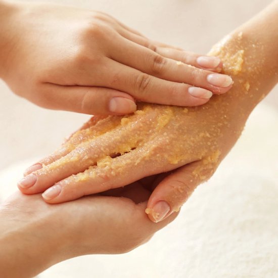 Een hand wordt ingemasseerd met een gele bodyscrub. De textuur van de scrub is zichtbaar.