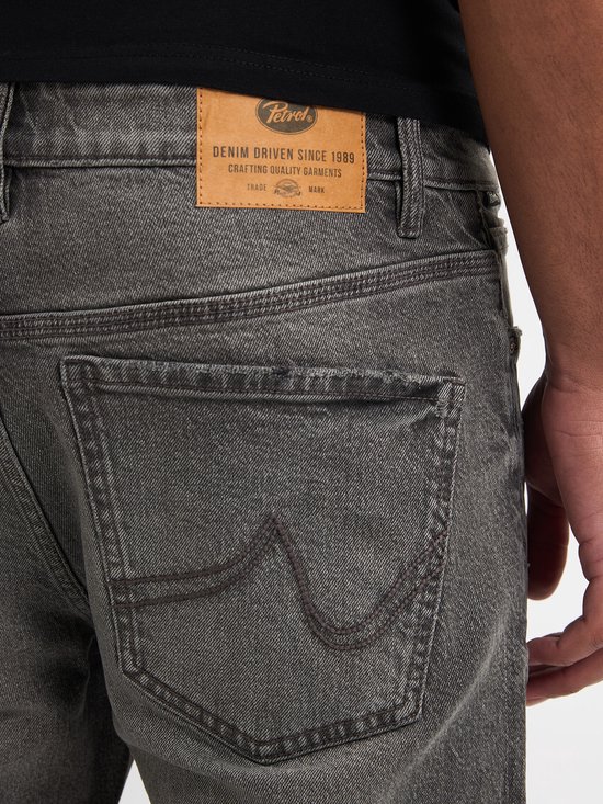 Achterkant van een grijze jeans met het 'Petrol' logo en 'Denim Driven Since 1989' tekst.