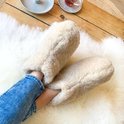 Damesbenen in spijkerbroek met beige wollen sloffen, zittend op een schapenvacht.