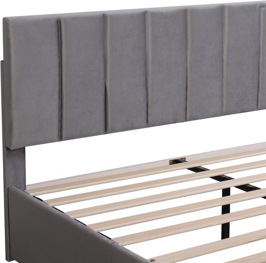 Grijze gestoffeerde hoofdsteun met verticale plooien en een deel van het bedframe met houten latten.