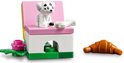 Een LEGO Friends hondje zit op een roze stoel met een bot. Een croissant ligt ernaast.