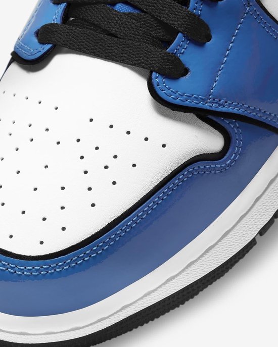 Close-up van de neus van een blauw-witte sneaker met perforaties in het witte leer en glanzende blauwe accenten.