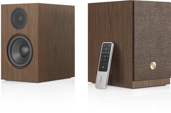 Paar boekenplankspeakers in walnoothout. Eén speaker heeft een zichtbare woofer en tweeter, de ander een stoffen frontpaneel. Een afstandsbediening staat tegen de laatste.
