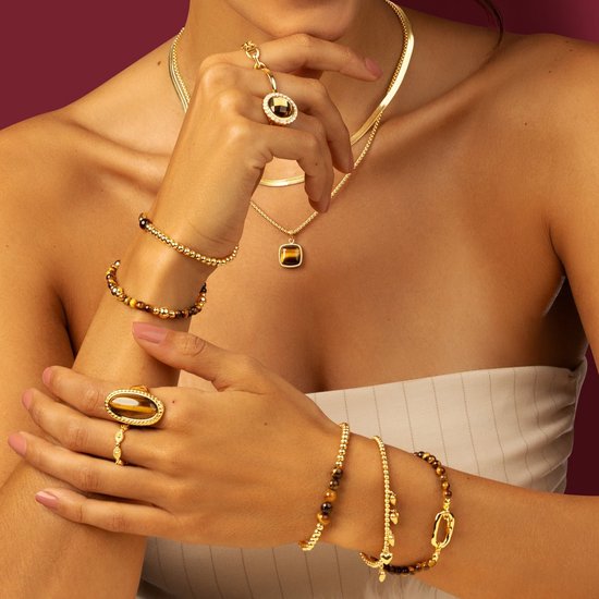 Mannequin portant des bijoux en or, y compris des bagues et des bracelets en œil de tigre et perles dorées.