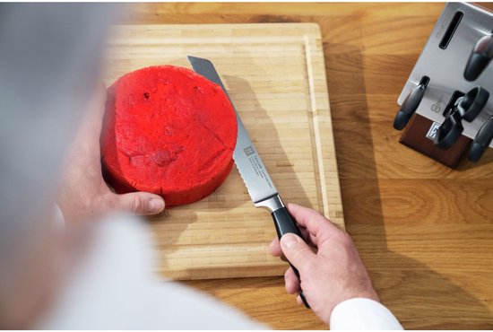 Handen snijden een rood, rond gebak met een kartelmes met zwart handvat.