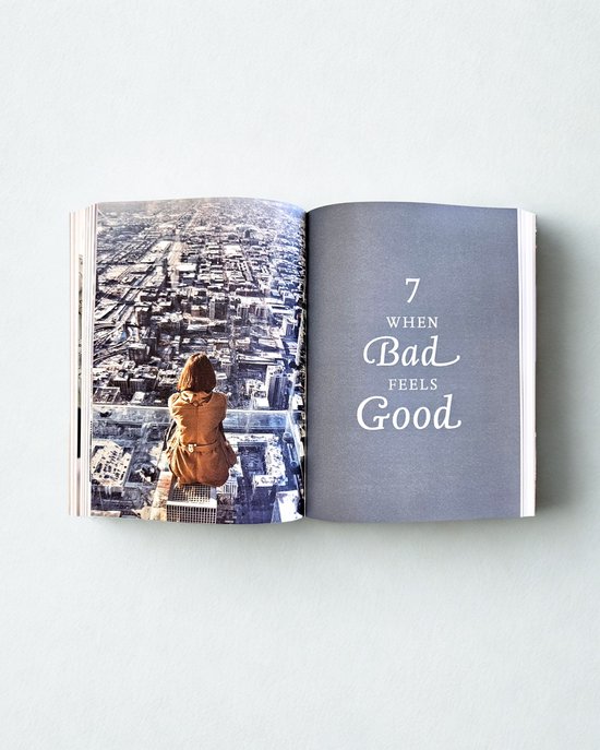 Een open boek toont een panoramisch uitzicht op een stad vanaf een glazen platform, met de tekst '7 WHEN Bad FEELS Good'.