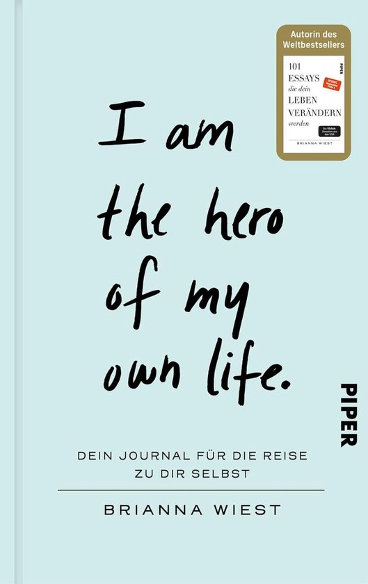 Boek met de titel 'I am the hero of my own life.' in handgeschreven letters. Ondertitel: 'Dein Journal für die Reise zu dir selbst'.