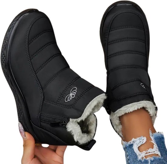 Bottes de neige noires matelassées avec doublure en fourrure blanche et fermeture éclair, présentées sur une personne.