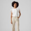 Femme portant un haut blanc court à volants et détails ajourés, et un pantalon cargo beige.
