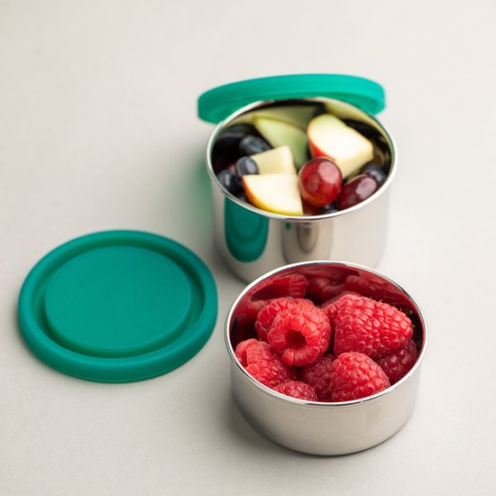 Deux boîtes rondes en acier inoxydable argenté avec couvercles verts. Une boîte contient des framboises, l'autre une salade de fruits.