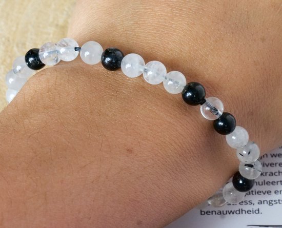 Armband met afwisselend zwarte toermalijn en heldere kwartskralen, gedragen om een pols.