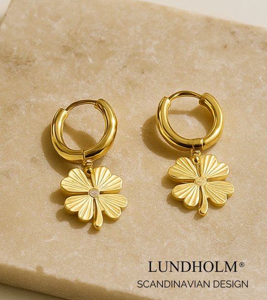 Boucles d'oreilles dorées avec pendentifs trèfle à quatre feuilles, avec pierre, sur une pierre claire.
