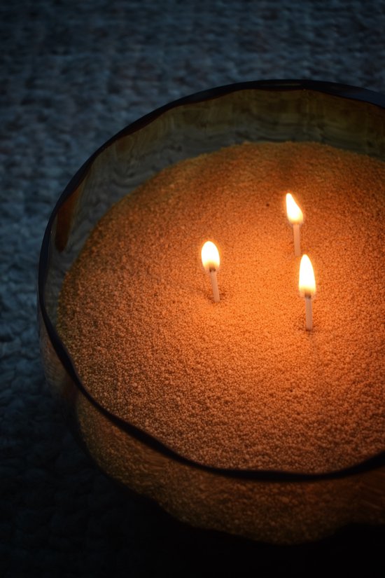 Een grote, oranje geurkaars in een glazen pot met drie brandende lonten.
