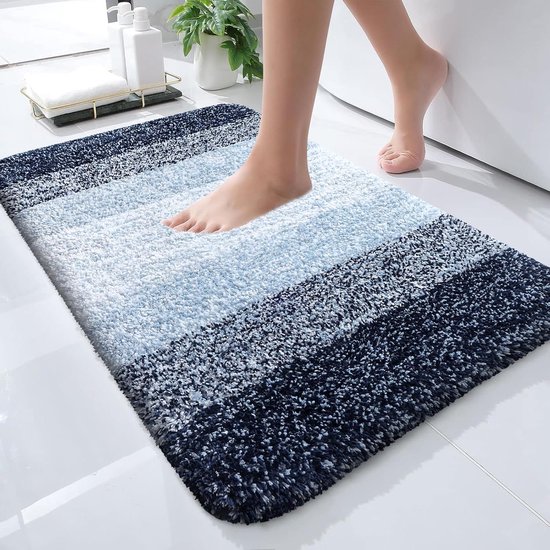 Voeten van een persoon die op een blauw-witte gestreepte badmat stappen, die voor een bad ligt. De mat is zacht en absorberend.
