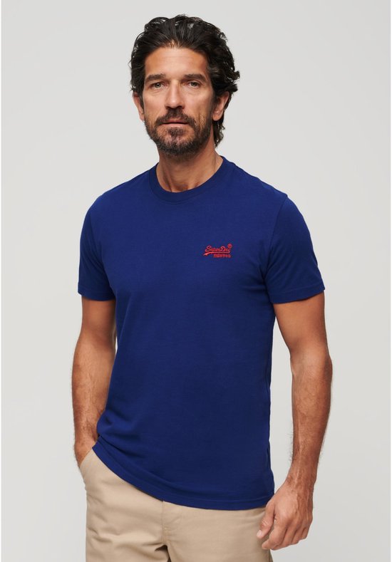 Homme portant un t-shirt bleu cobalt avec logo Superdry rouge sur la poitrine et un pantalon beige.