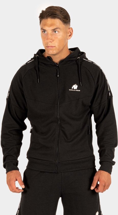 Man met spierbundel met een zwarte trainingsjas van Gorilla Wear, met tape op de schouders en mouwen.