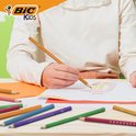 Kind tekent met een oranje Bic Kids potlood een afbeelding van een jaguar, met diverse gekleurde potloden op de voorgrond.