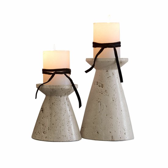 Twee beige kandelaars met zwarte linten en witte kaarsen, staand op een donker oppervlak.