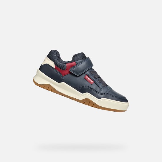 Donkerblauwe sneaker met rode en witte accenten, beige zool, van de zijkant gezien.
