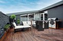 Zwart droogrek met kleding op een houten terras, met loungeset en barbecue.