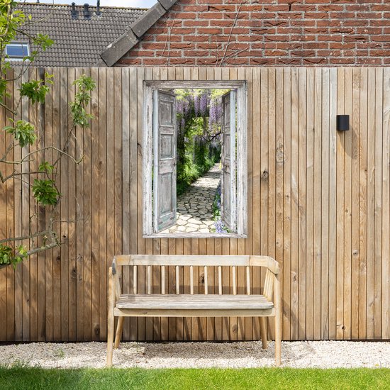 Een tuinposter met een doorkijk door een open deur naar een bloeiend pad, geplaatst tegen een houten schutting boven een houten bankje.