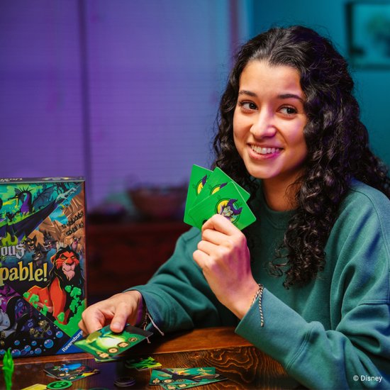 Vrouw met krullend haar speelt Disney Villainous Unstoppable en houdt groene kaarten vast.