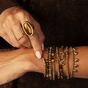 Model draagt een gouden ring met tijgeroog en een gouden schakelarmband, een gouden kralenarmband en een gouden armband met hartjes.