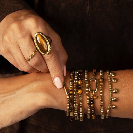 Model draagt een gouden ring met tijgeroog en een gouden schakelarmband, een gouden kralenarmband en een gouden armband met hartjes.