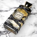 Oud Mood parfumfles met gouden dop, omwikkeld met zwart lint met "Oud Mood" erop, op een marmeren ondergrond.