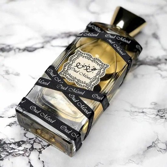 Oud Mood parfumfles met gouden dop, omwikkeld met zwart lint met "Oud Mood" erop, op een marmeren ondergrond.