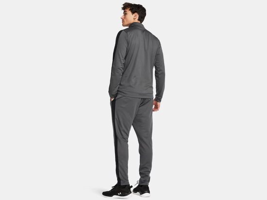Achterkant van een man in grijs Under Armour trainingspak met zwarte streep op het been en de mouw.