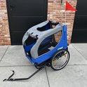 Blauwe fietskar met grijze kap, voorste instapopening en rood vlaggetje.