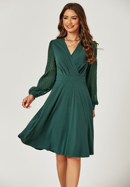 Model in een donkergroene midi-jurk met wikkelkraag en pofmouwen met stippen. De jurk heeft een A-lijn rok.